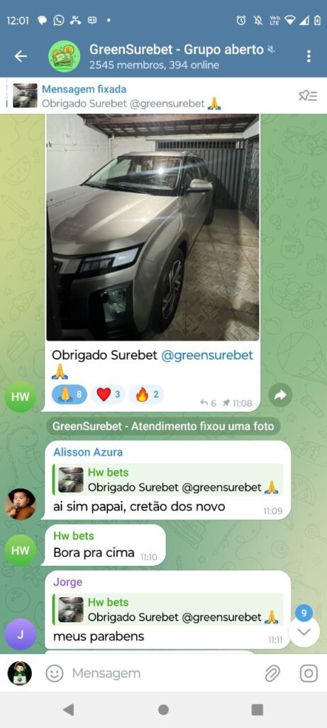 Foto de um carro prateado estacionado em uma garagem, com uma conversa do grupo GreenSurebet no WhatsApp ao fundo.